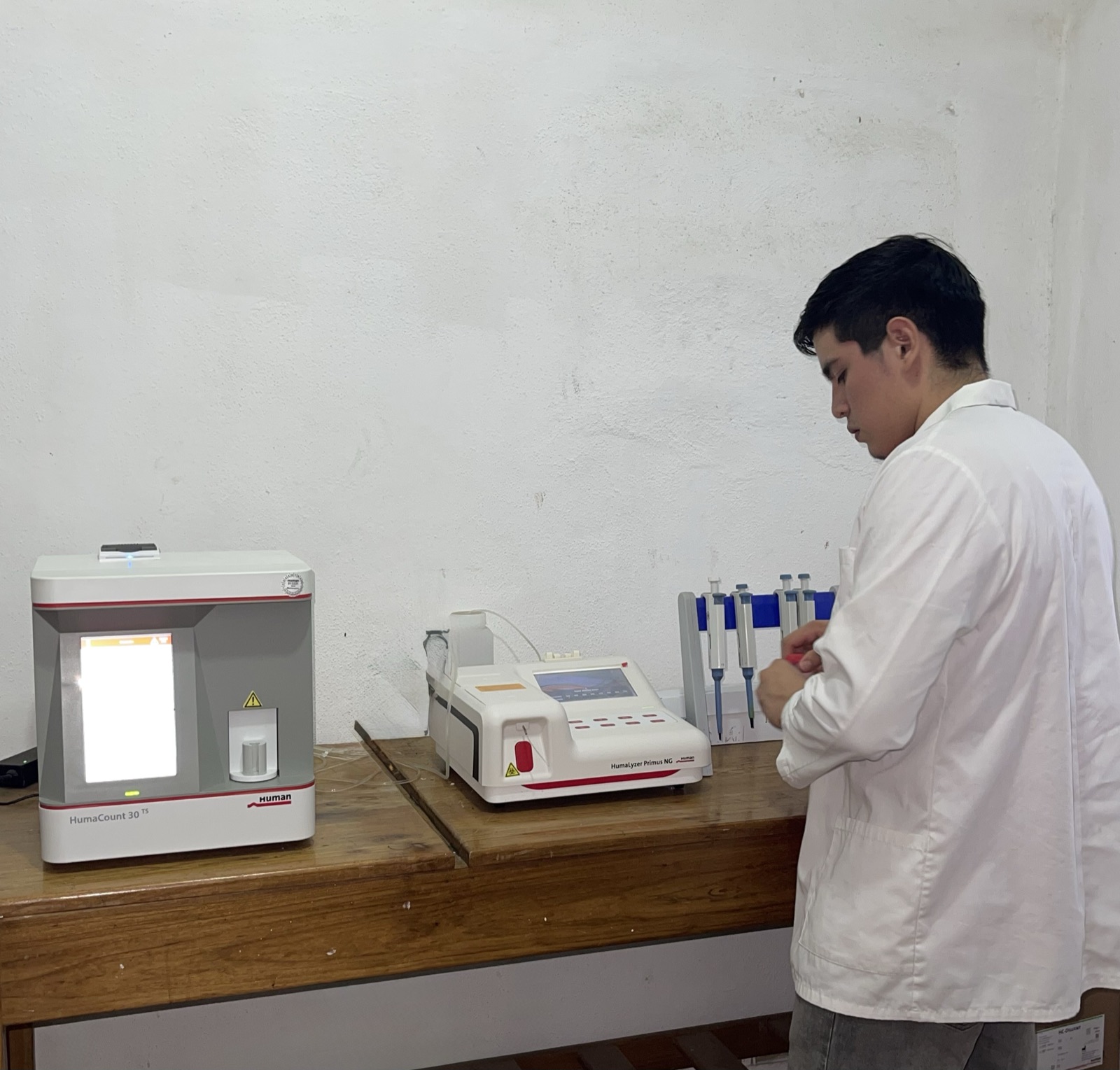 Estación de trabajo del laboratorio con el HumaCount 30 TS, el HumaLyzer Primus NG y micropipetas sobre una mesa de madera, junto a un integrante del equipo con bata blanca