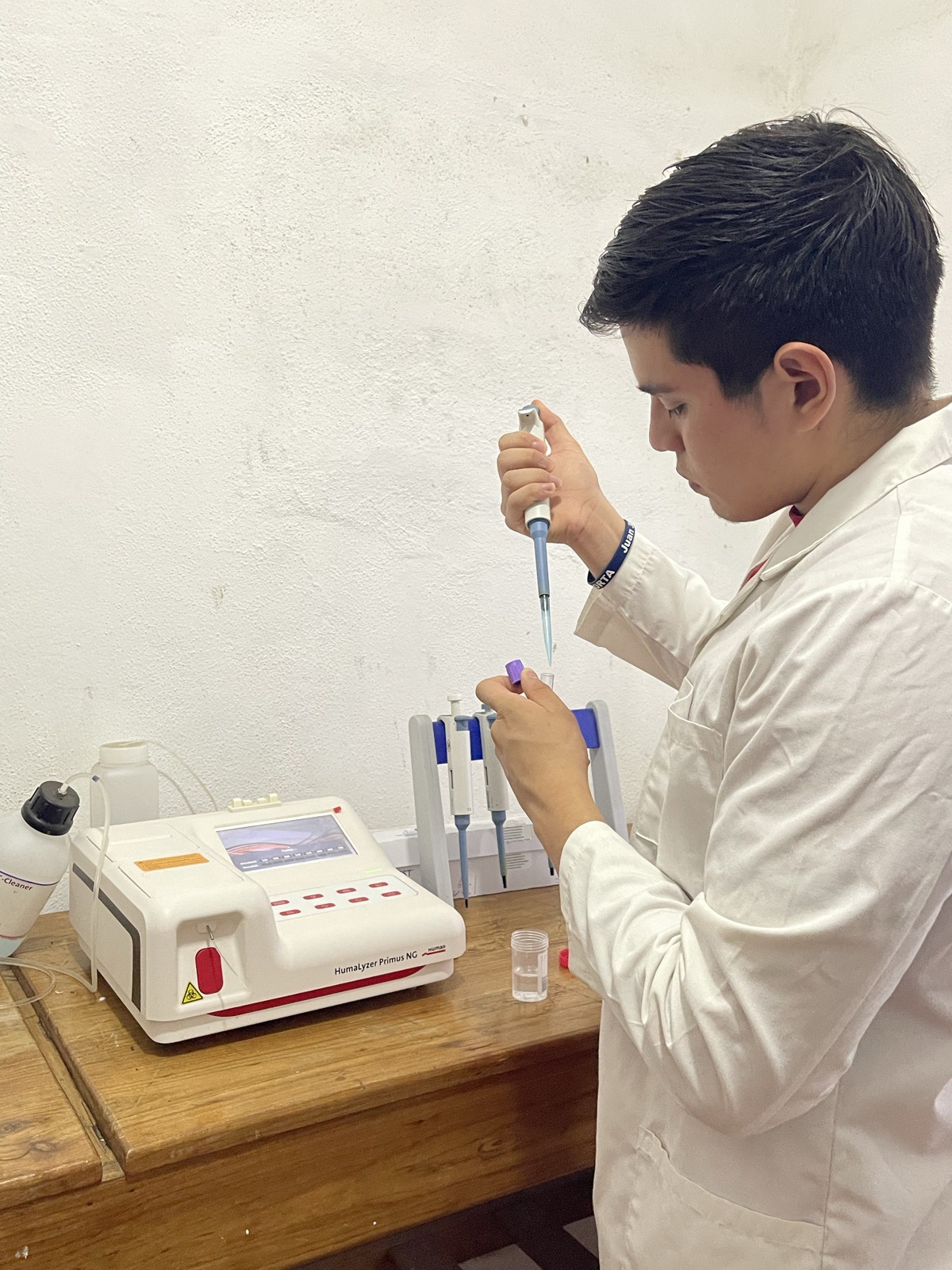 Integrante del equipo con bata blanca usando una micropipeta junto al analizador bioquímico HumaLyzer Primus NG